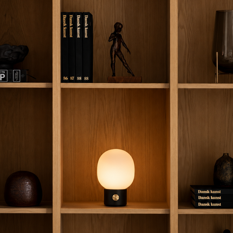 Warm-glowing frosted glass mushroom table lamp with black metal base and brass dimmer, set inside wooden shelf cubby.