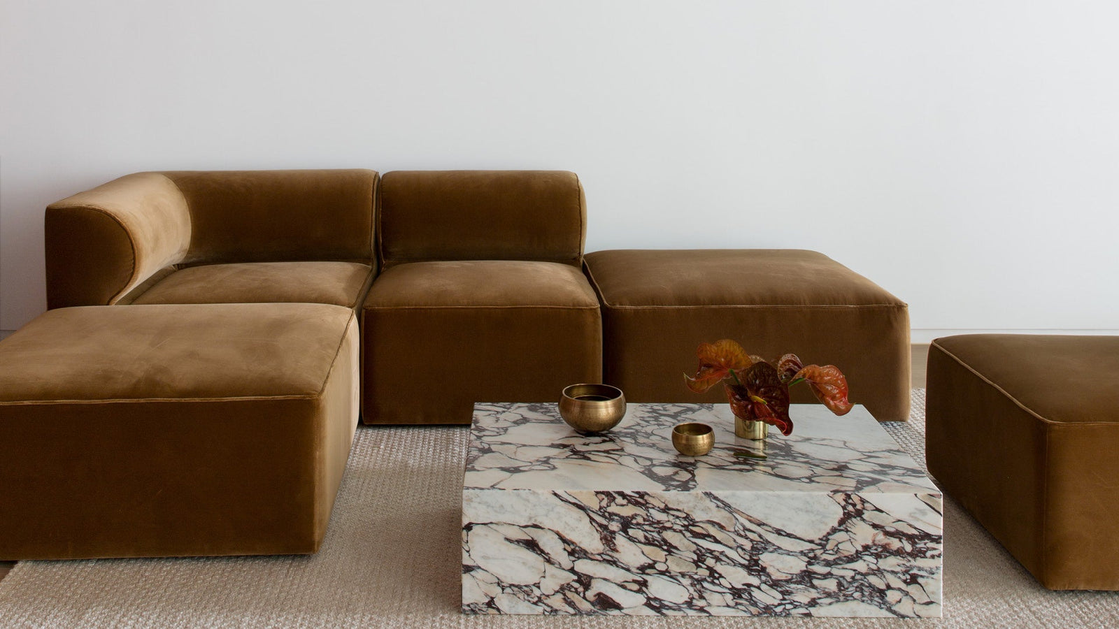 Modular brown velvet sectional with rounded cushions and marble low coffee table with brass bowls and vase