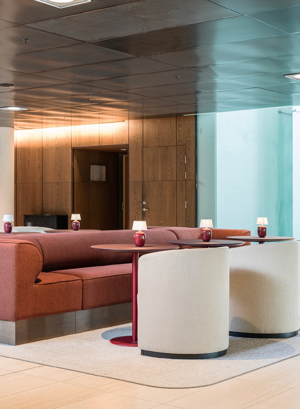 Contemporary lounge with curved red upholstered sofa, beige fabric swivel chairs, round red tables and small red table lamps