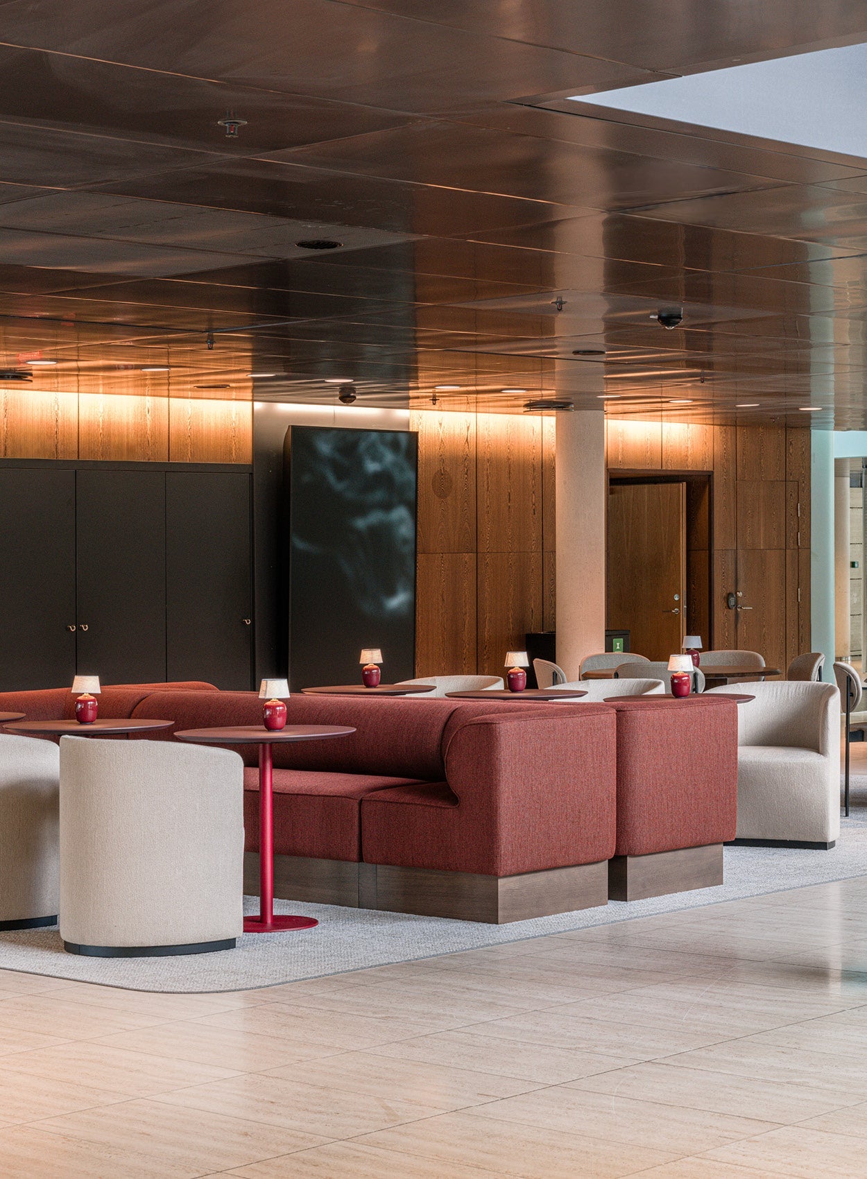 Contemporary lounge with curved red fabric sofas, beige armchairs, red round tables and warm wood-paneled walls and ceiling