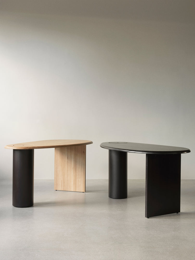 Two minimalist kidney-shaped side tables, one light oak top with black cylindrical leg and oak panel, one black top with