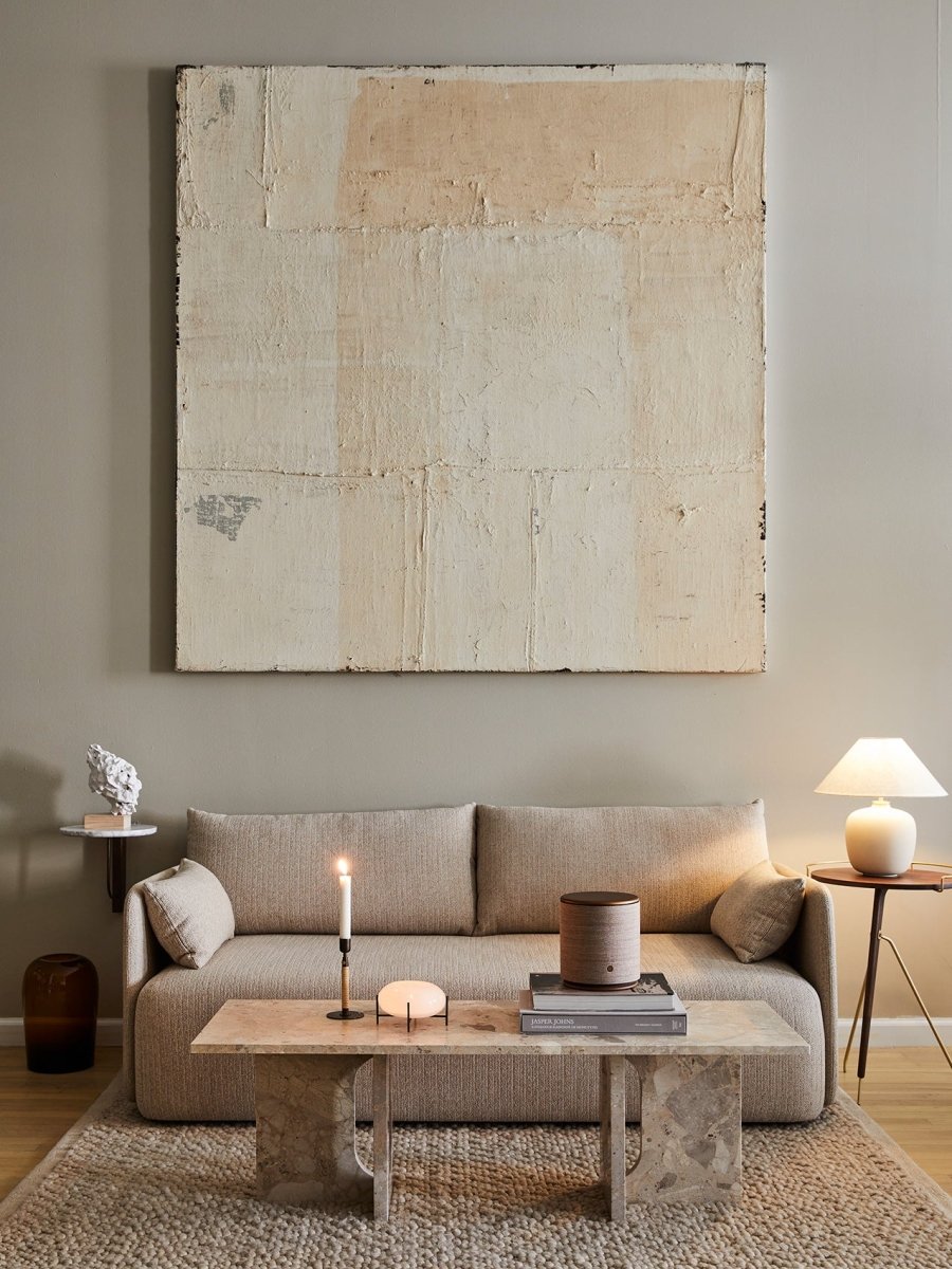 Neutral-toned living room with beige textured sofa, large abstract cream canvas, travertine coffee table, candle and ceramic