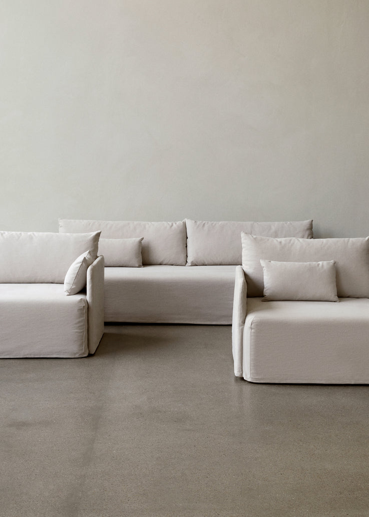 Modular off-white linen sofa set with boxy cushions and low arms, arranged on polished concrete floor against pale wall