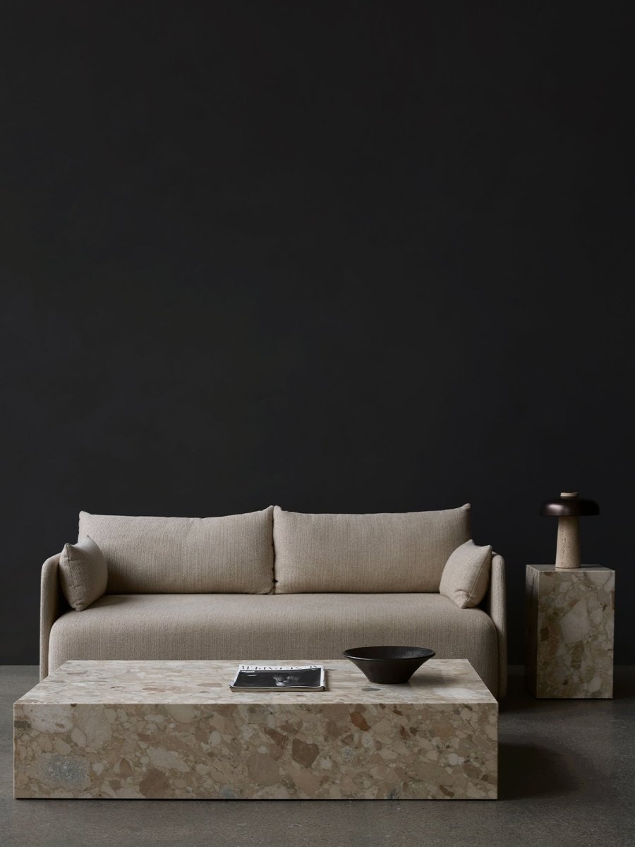 Beige upholstered two-seat sofa with cylindrical arm cushions, marble block coffee table and side pedestal with dark lamp