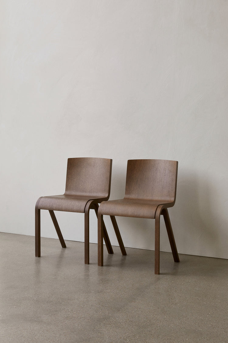 Pair of molded bentwood dining chairs in warm walnut finish with curved seats and angled legs against pale wall