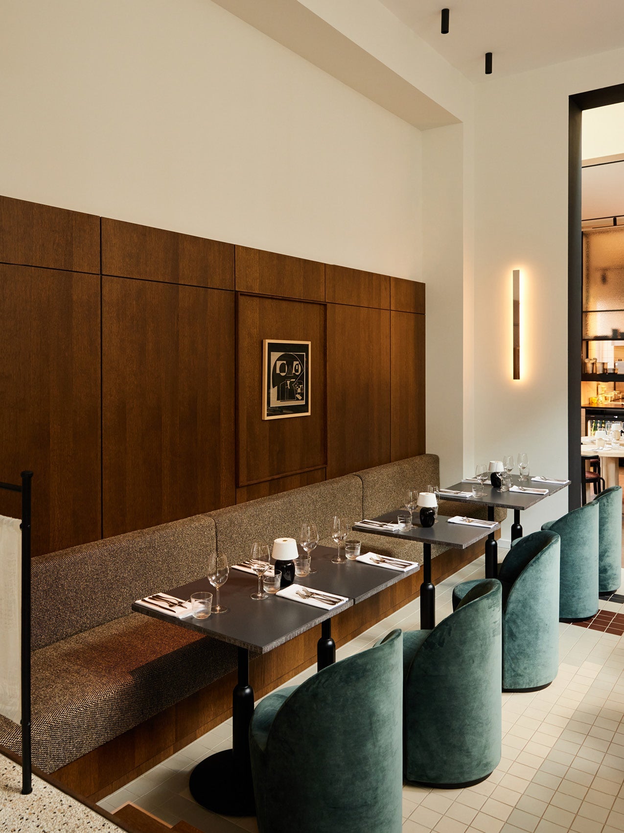 Restaurant booth with dark wood paneling, grey upholstered bench, black stone tables and teal velvet curved chairs, wall