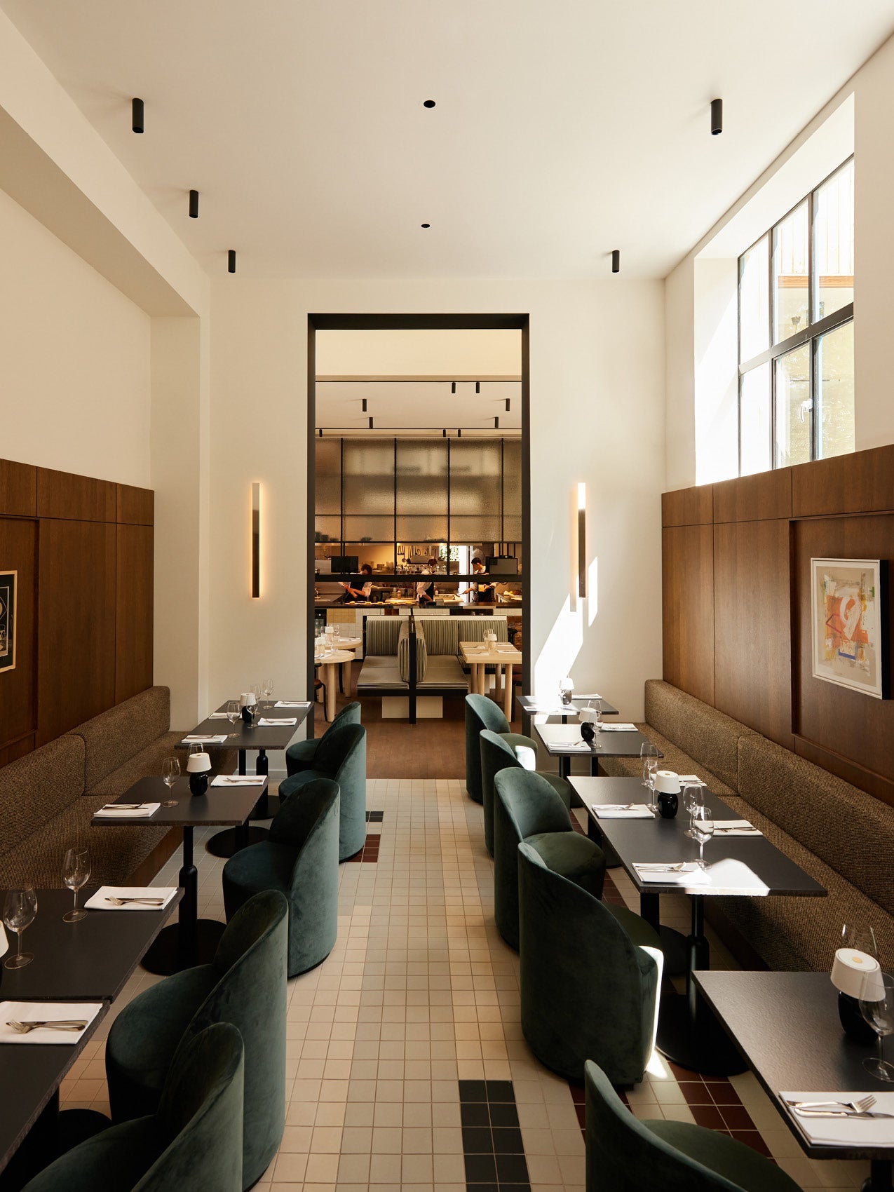 Minimalist restaurant interior with dark green velvet curved chairs, black tables, wood-paneled walls and tiled floor