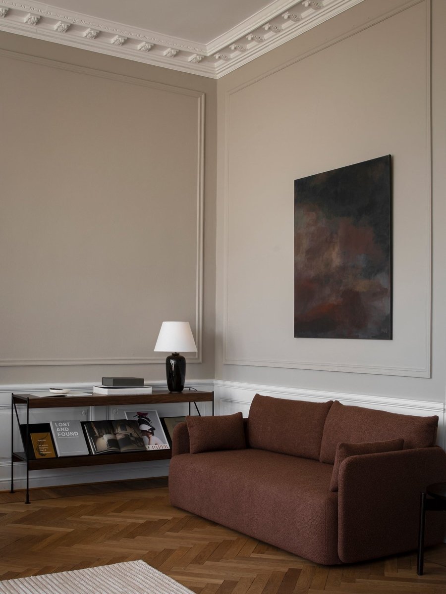 Minimal living room corner with a brown textured fabric sofa, dark wood console with black ceramic lamp, abstract wall