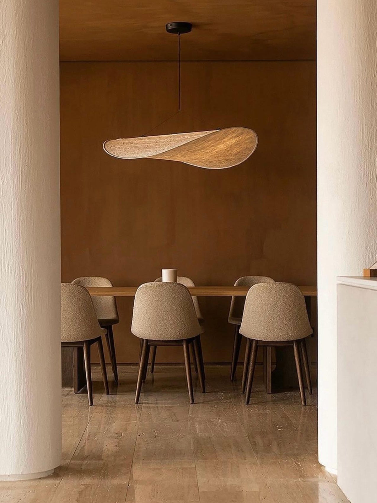 Minimal dining room with curved beige upholstered chairs, wooden table and organic-shaped woven pendant light in warm tones.