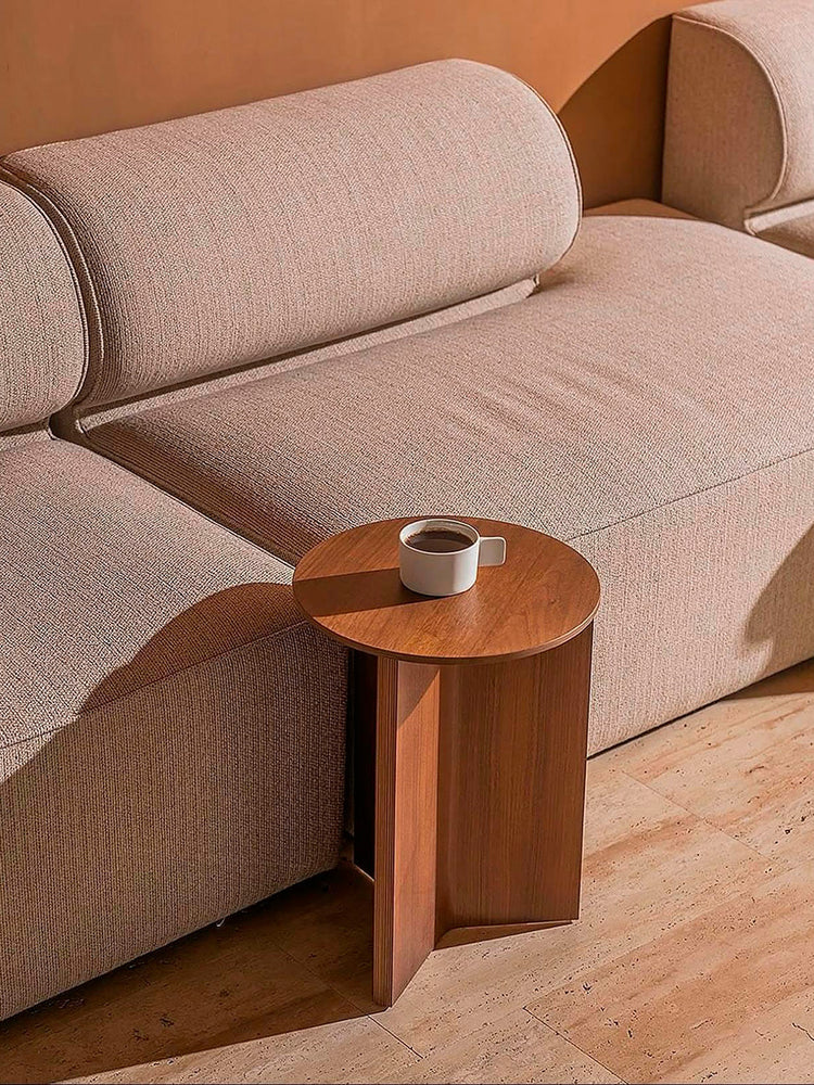 Beige textured fabric sofa with rounded back cushions and a small round wooden side table holding a white coffee cup