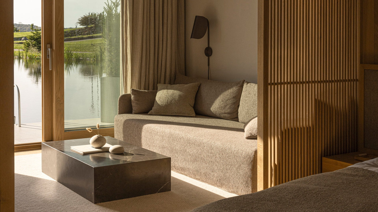 Cozy beige boucle sofa with matching cushions, dark rectangular marble coffee table and wooden slatted room divider by glass