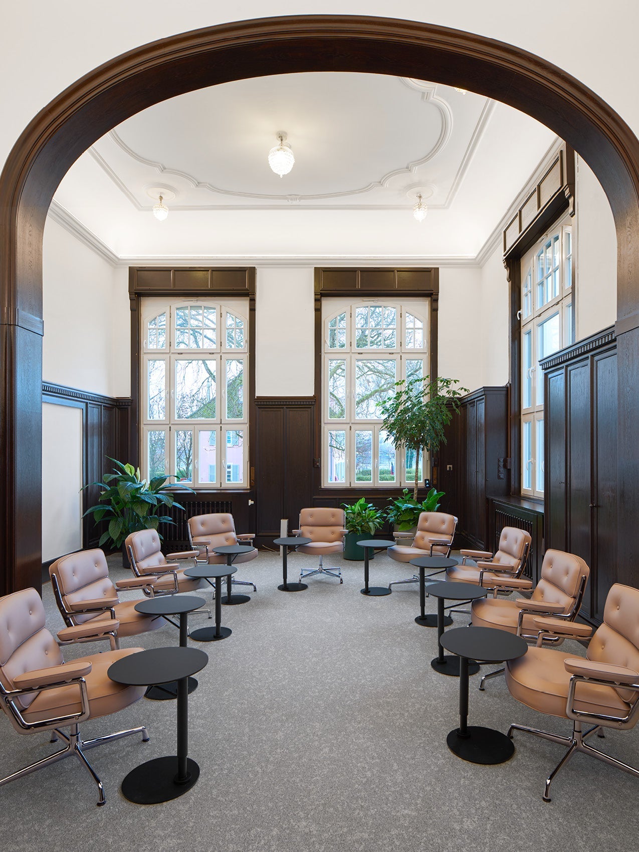 Spacious meeting room with arched wood doorway, tan leather swivel chairs, black round side tables and tall arched windows