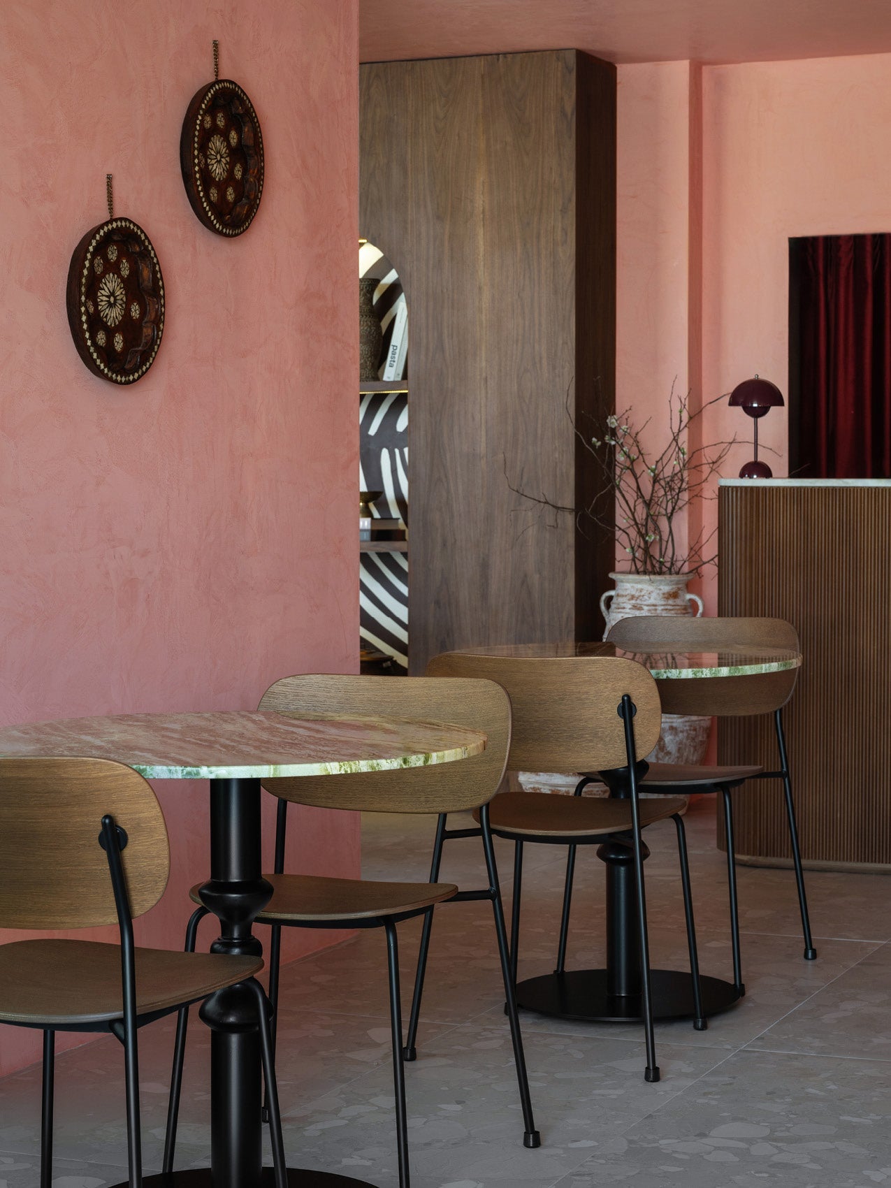 Café scene with round green-veined marble tables, wooden chairs with black metal legs, pink plaster walls and decorative