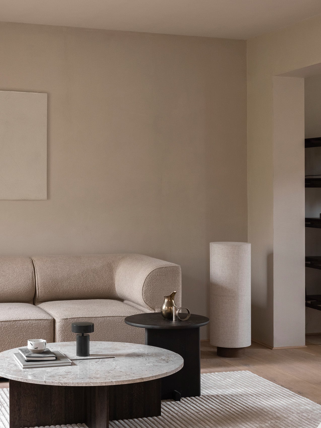 Minimal beige boucle sofa and round marble-top coffee table with black side table and brass pitcher.