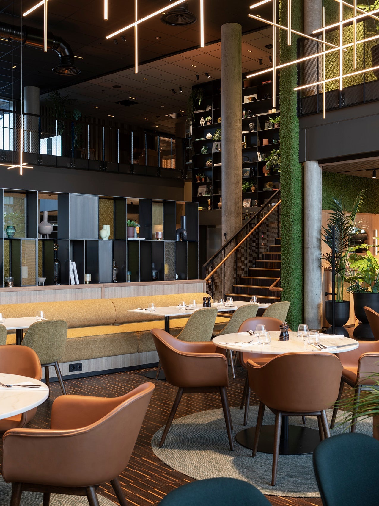 Modern hotel restaurant interior with tan leather armchairs, marble tables, mustard banquette, metal shelving and vertical