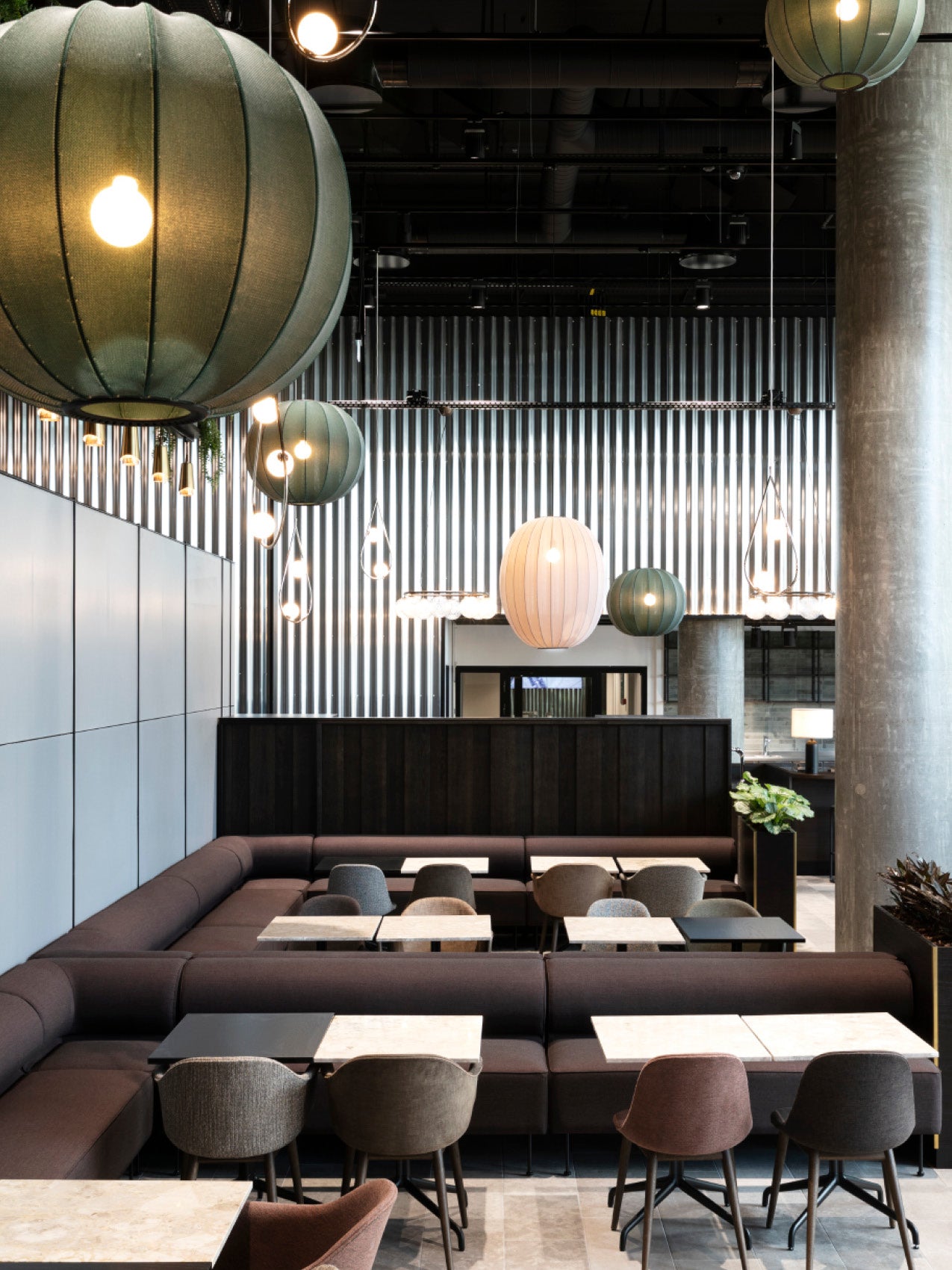 Modern dining lounge with dark upholstered banquettes, marble tables and hanging spherical fabric pendant lights in green