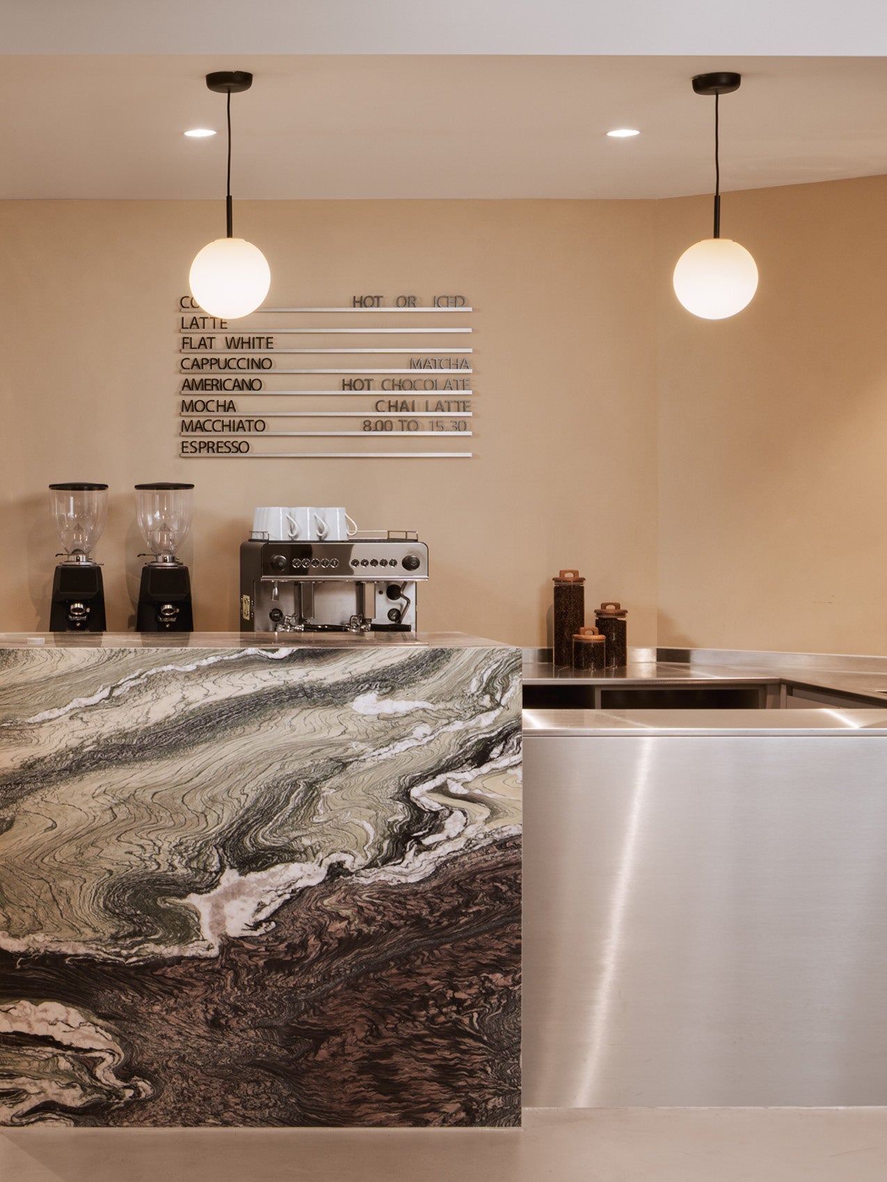 Minimal cafe counter with green and brown marble front, stainless steel side, espresso machine, grinders and two round
