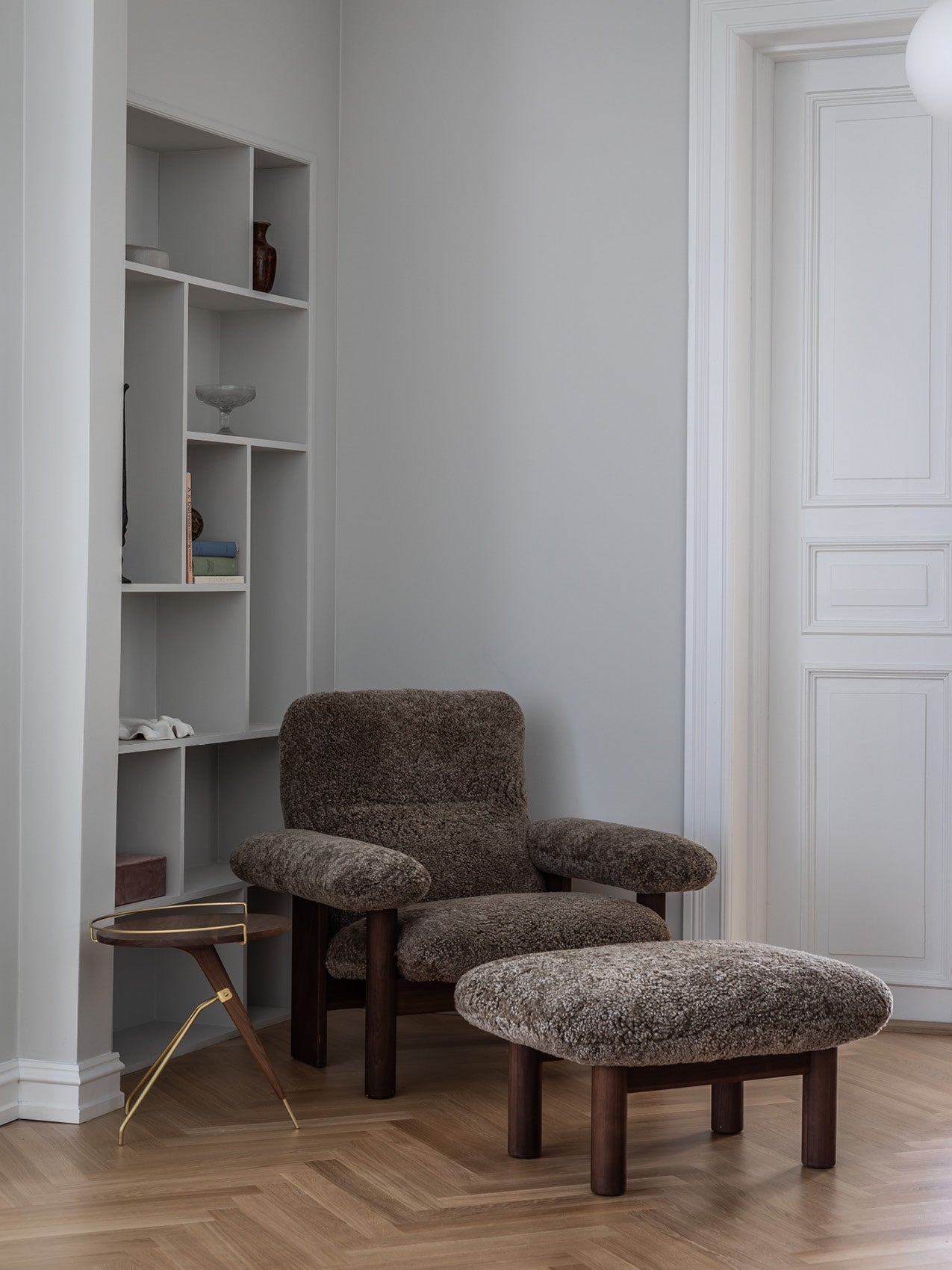 Plush brown sheepskin armchair and matching ottoman with dark wooden legs beside a small brass-accented side table and