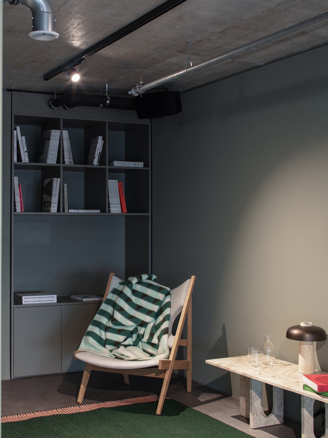 Scandinavian wooden lounge chair with light grey fabric and green striped wool blanket beside marble side table and matte