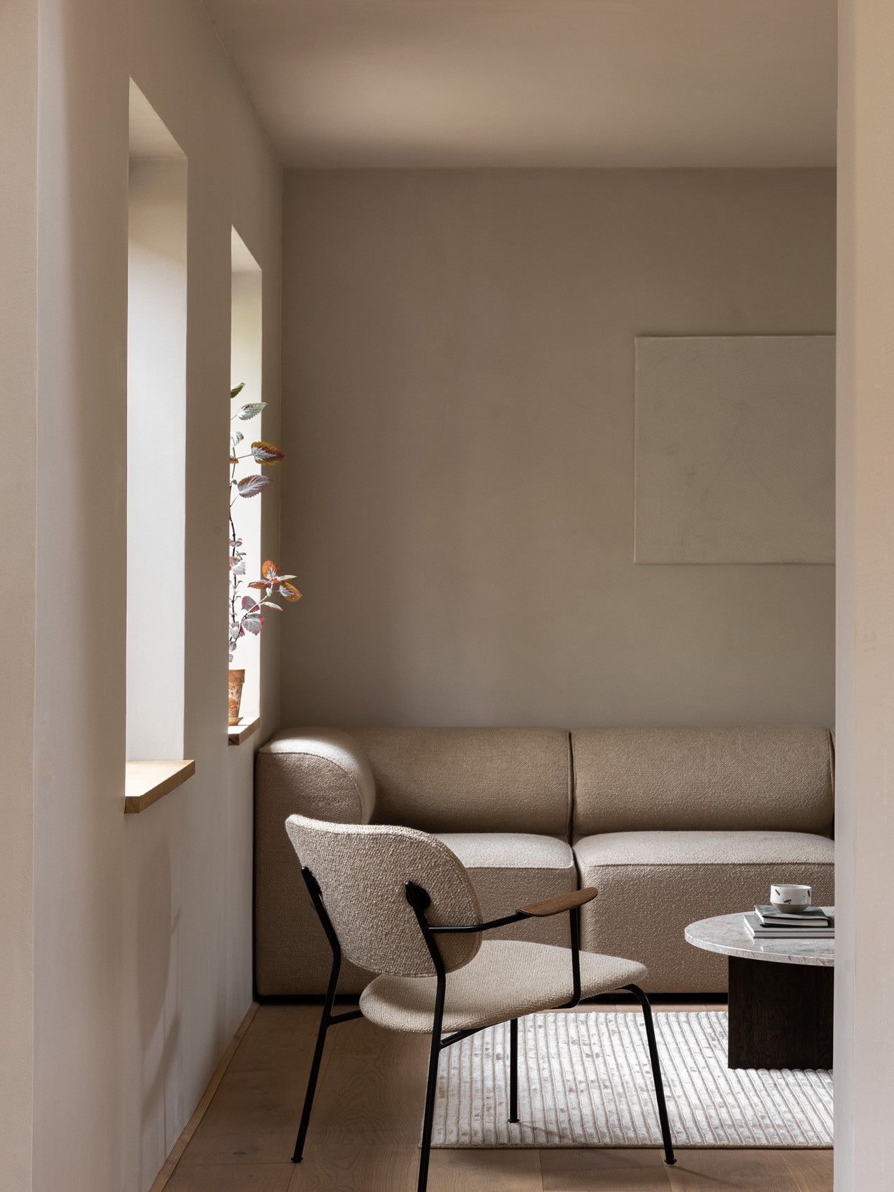Minimal living room with beige boucle sofa and matching armless lounge chair with black metal frame, round marble side table