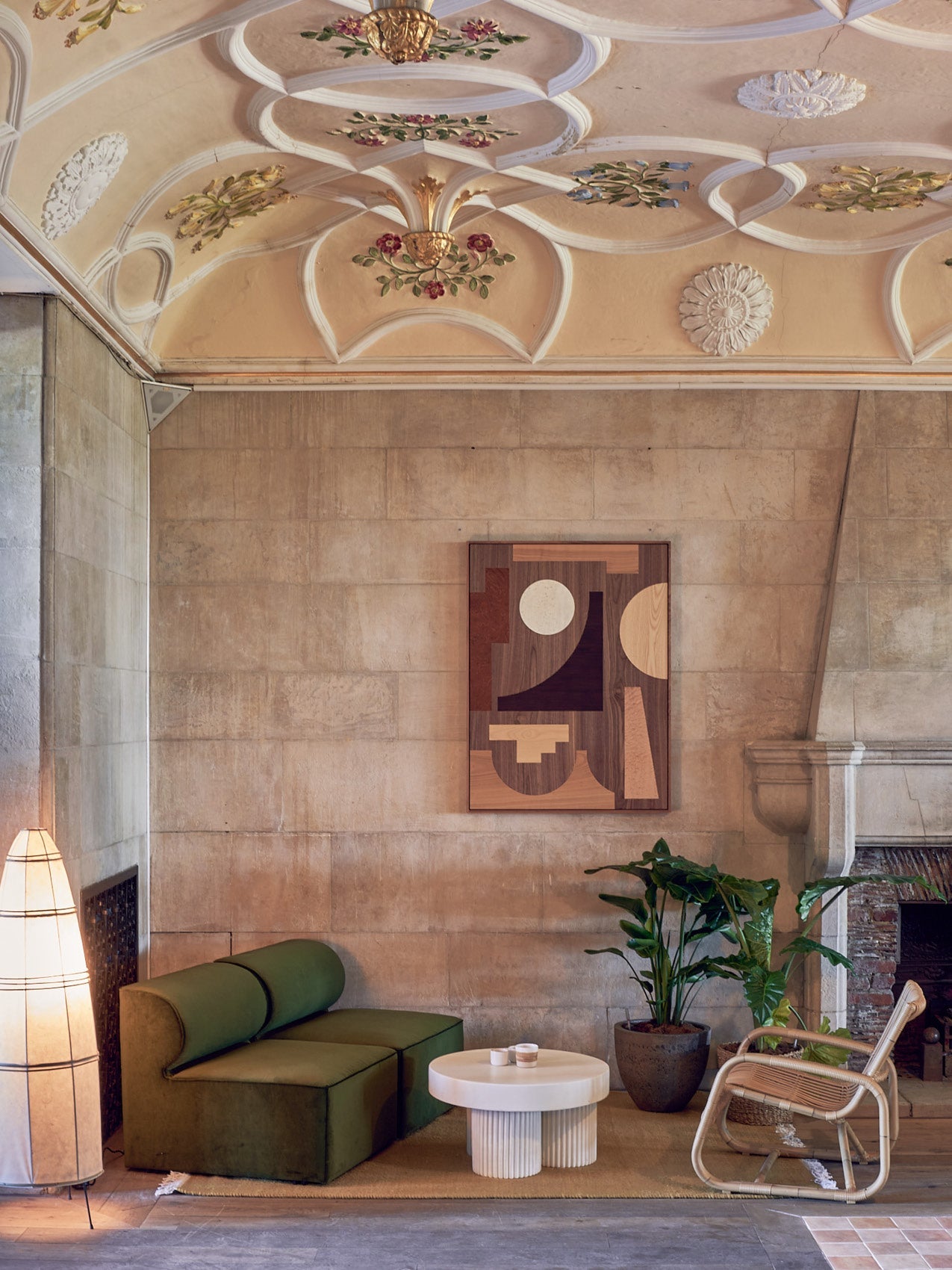 Cozy seating corner with olive green modular sofa, round fluted white coffee table, rattan chair, potted plant, stone wall
