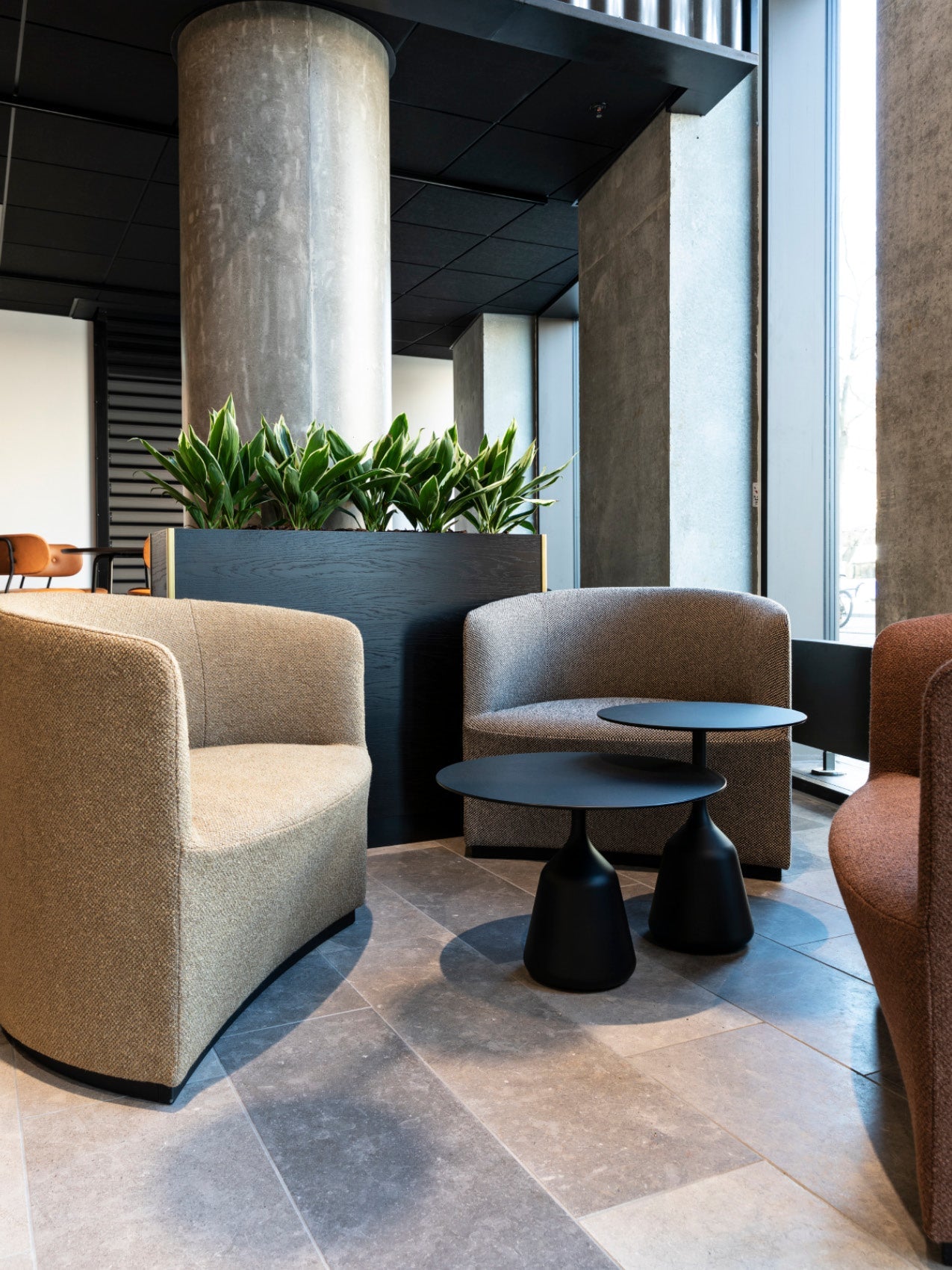 Curved beige and gray upholstered lounge chairs around two matte black nesting side tables with planter and concrete column