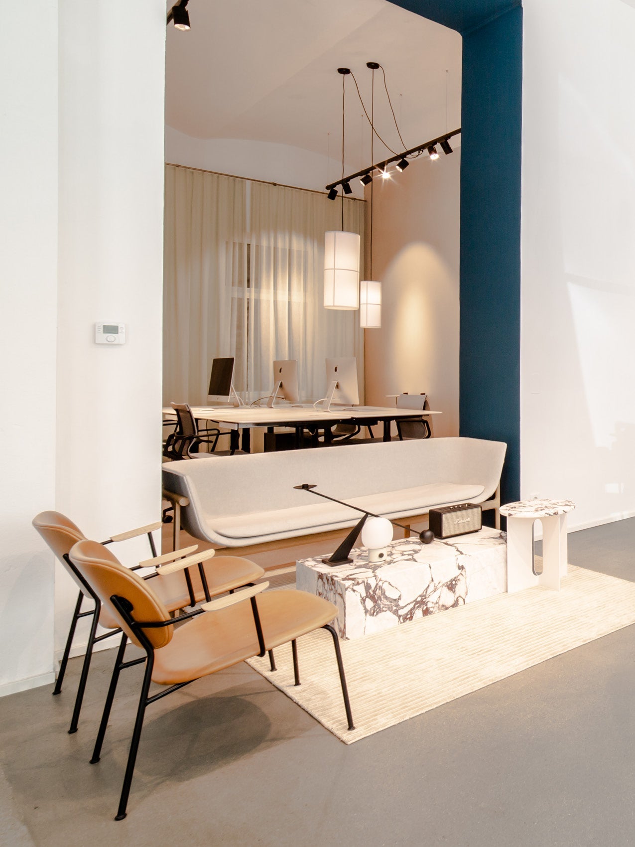Minimal showroom seating area with beige curved sofa, tan leather chairs, marble low table and pendant lights above