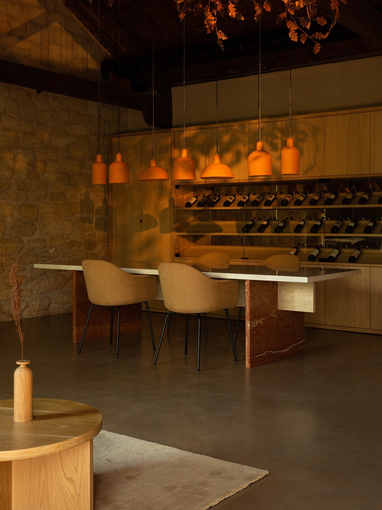 Warm dining area with terracotta pendant lamps, tan upholstered chairs, marble table legs and wooden wine rack backdrop