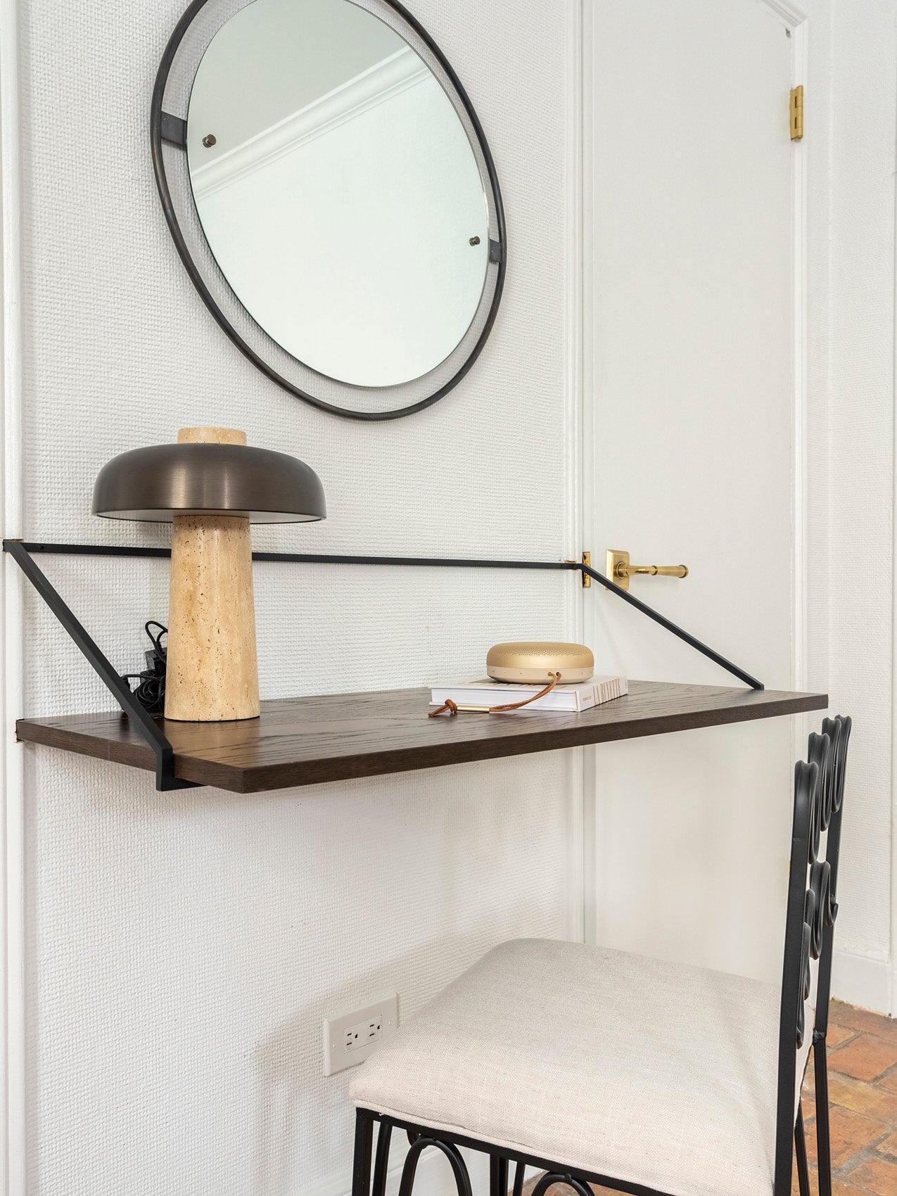 Wall-mounted dark wood shelf with black metal brackets, beige stone lamp with bronze dome shade and round mirror above.