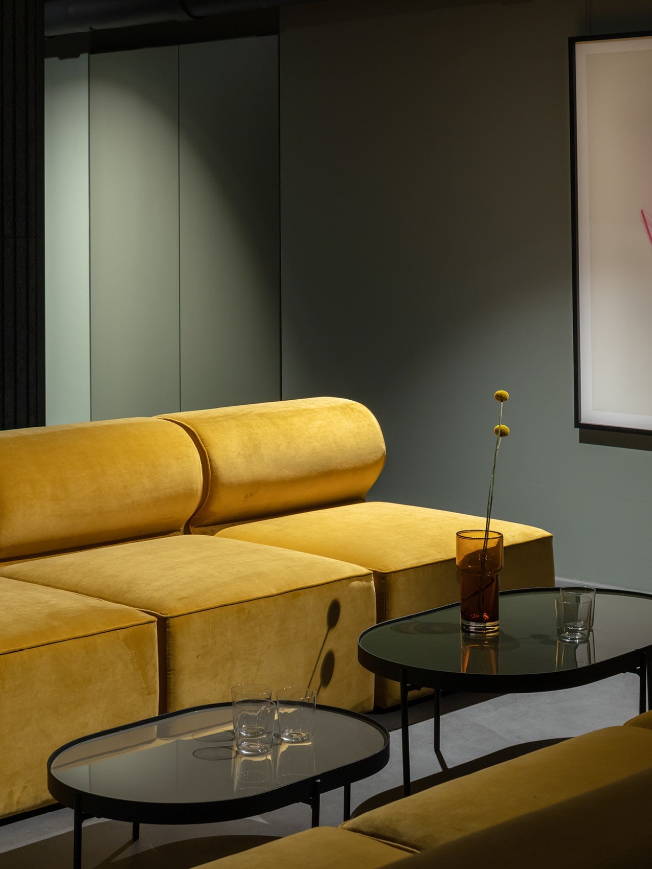 Mustard yellow velvet modular sofa with rounded back cushions beside black glass nesting coffee tables and amber vase