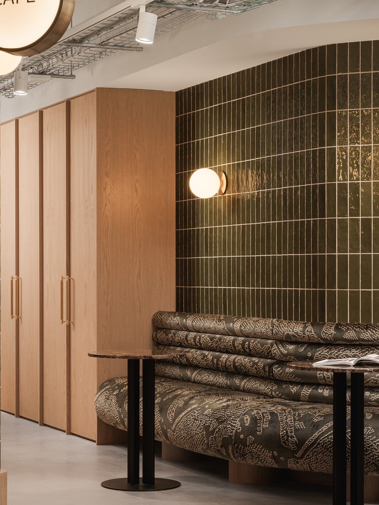 Curved dark green tiled wall with brass round wall light, oak panel cabinets and patterned upholstered bench with black