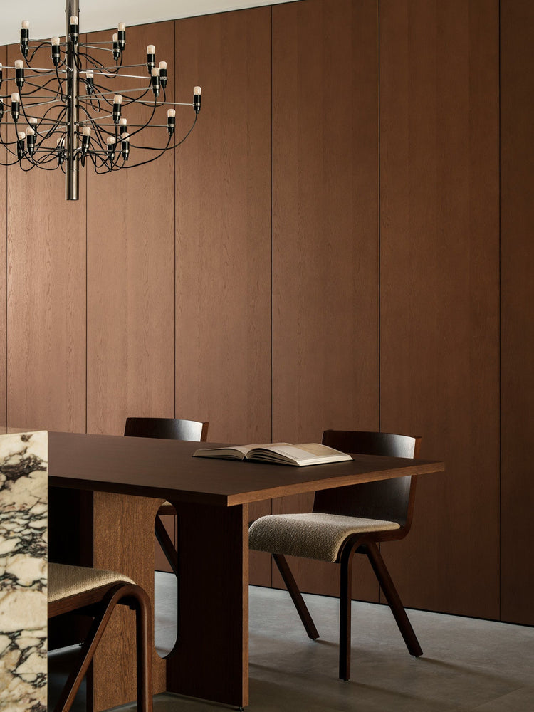 Dark wood dining table and chairs with upholstered seats, open book on table, marble counter edge and black multi-bulb