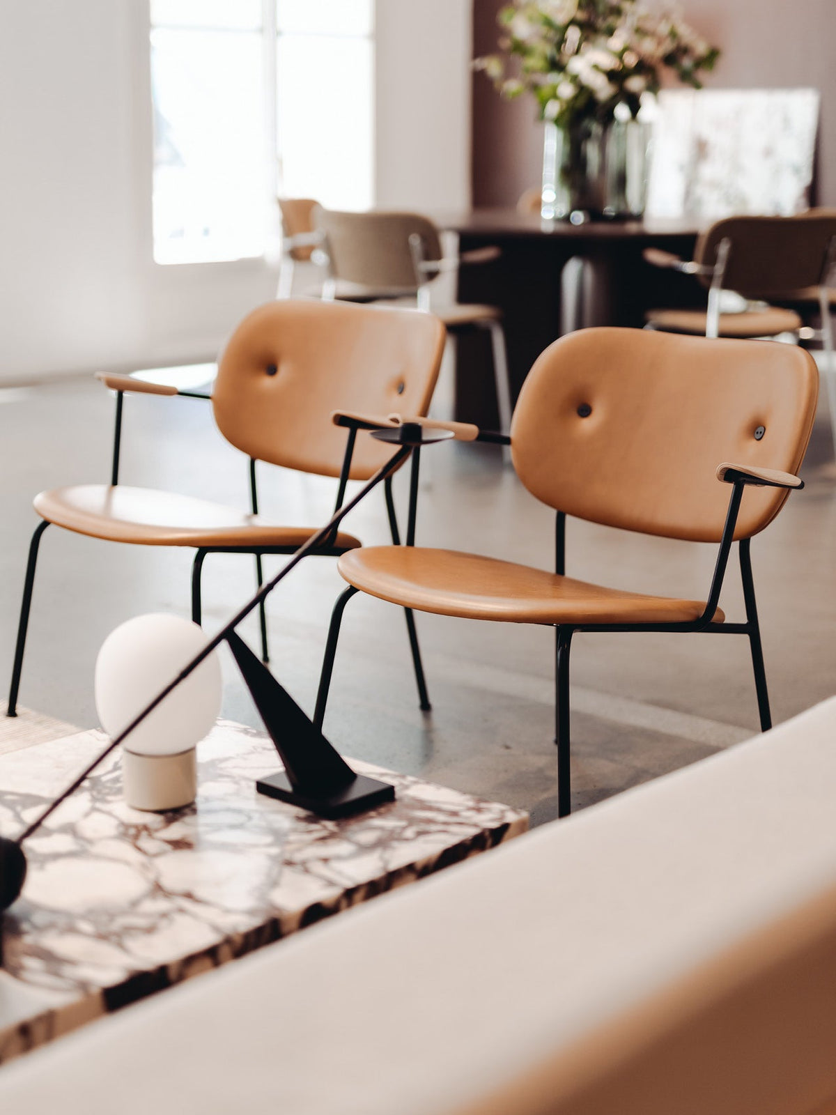Tan leather and black metal armchairs with button details in a sophisticated living room setting featuring a marble table.