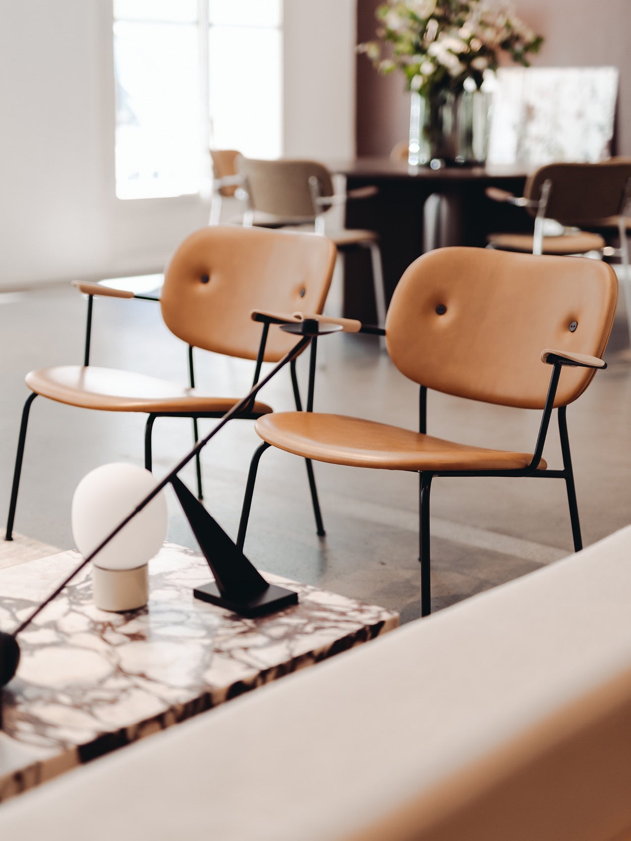 Pair of tan leather lounge chairs with rounded seats and buttoned backs on slim black metal frames.