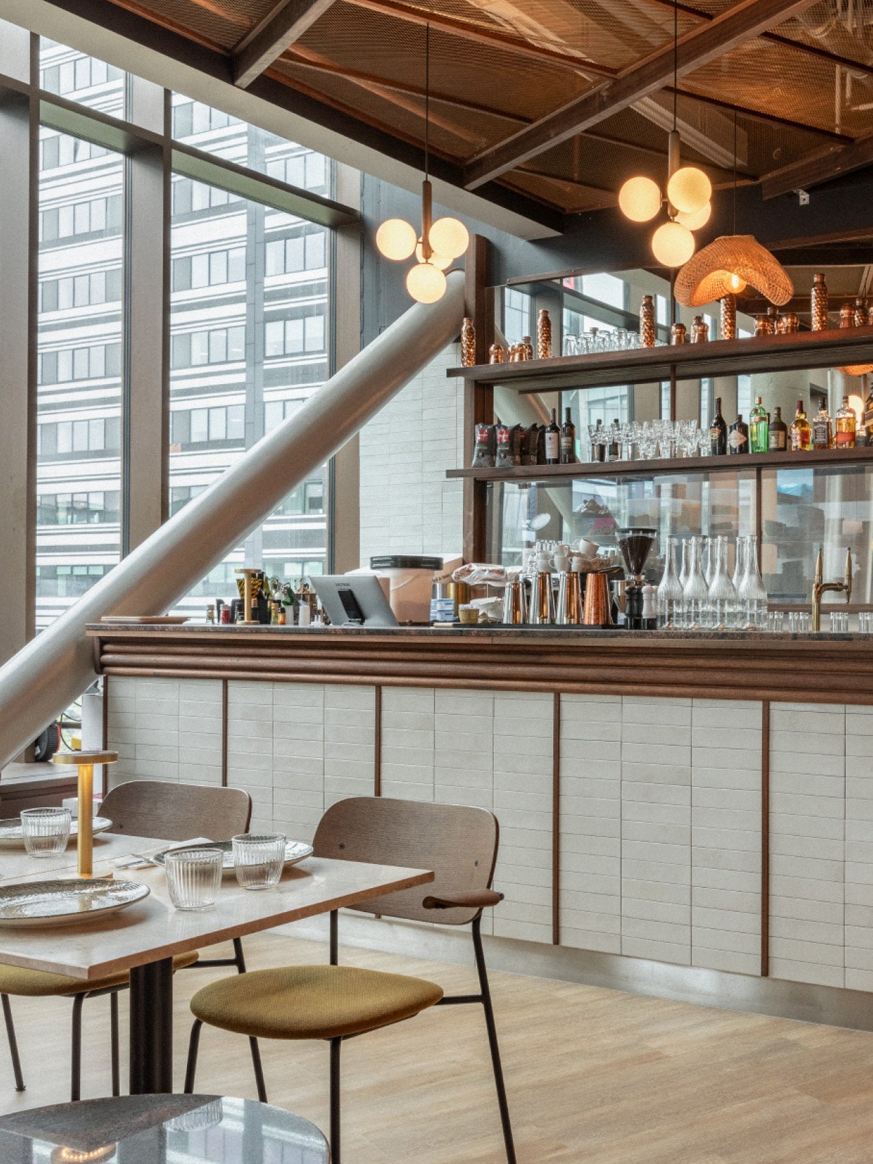 Modern café bar interior with wooden counter, white tile front, pendant globe lights and glassware on shelves.