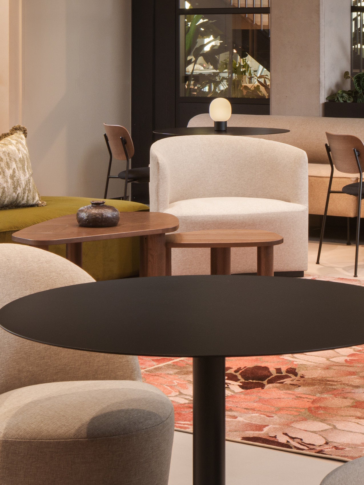 Modern lounge setting with beige curved upholstered armchairs, black round table, wooden nesting tables and small lamp