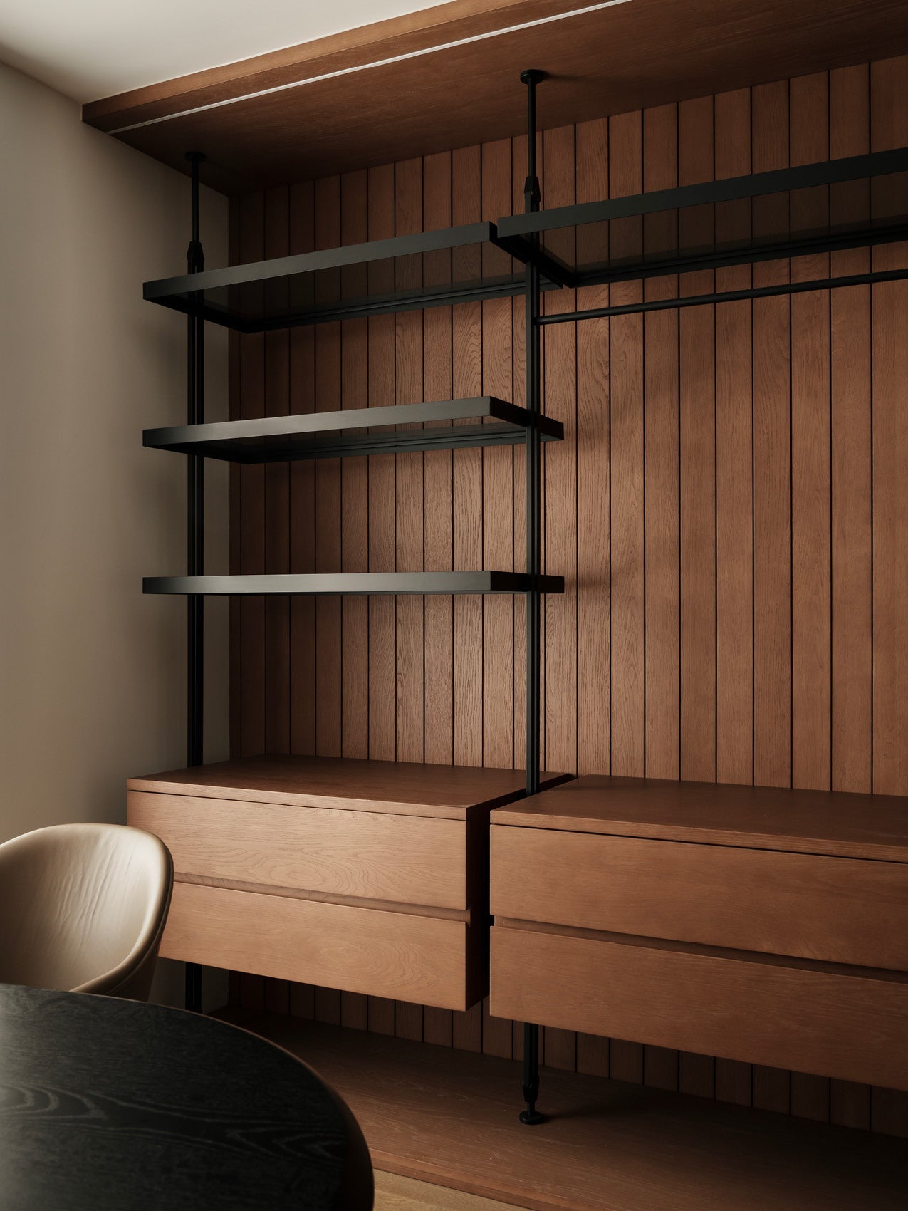 Wall-mounted black metal shelving with three dark shelves above paired warm oak floating drawers against vertical wood
