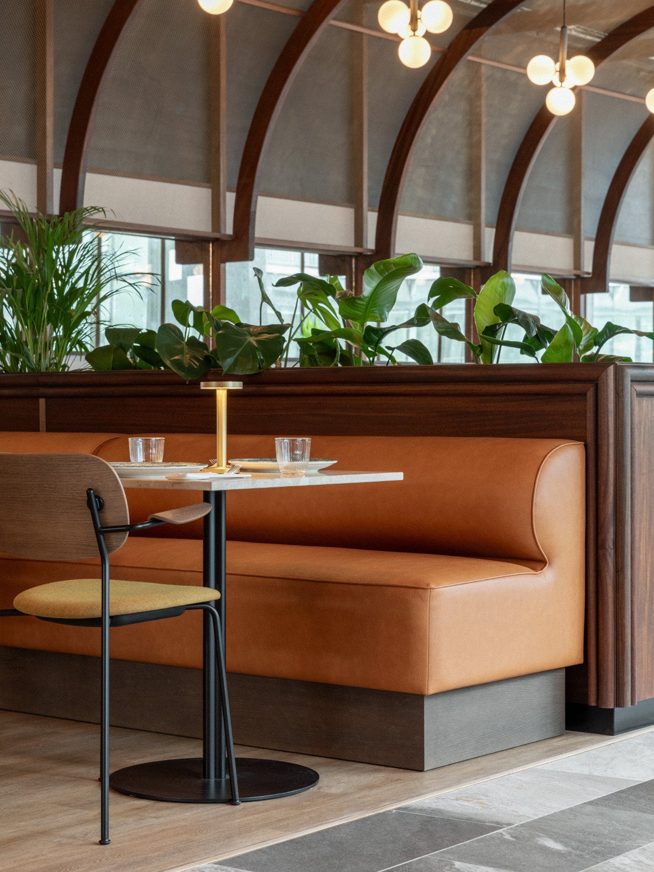 Leather banquette in warm tan beside marble-top table, black metal chair and brass table lamp with leafy planter backdrop