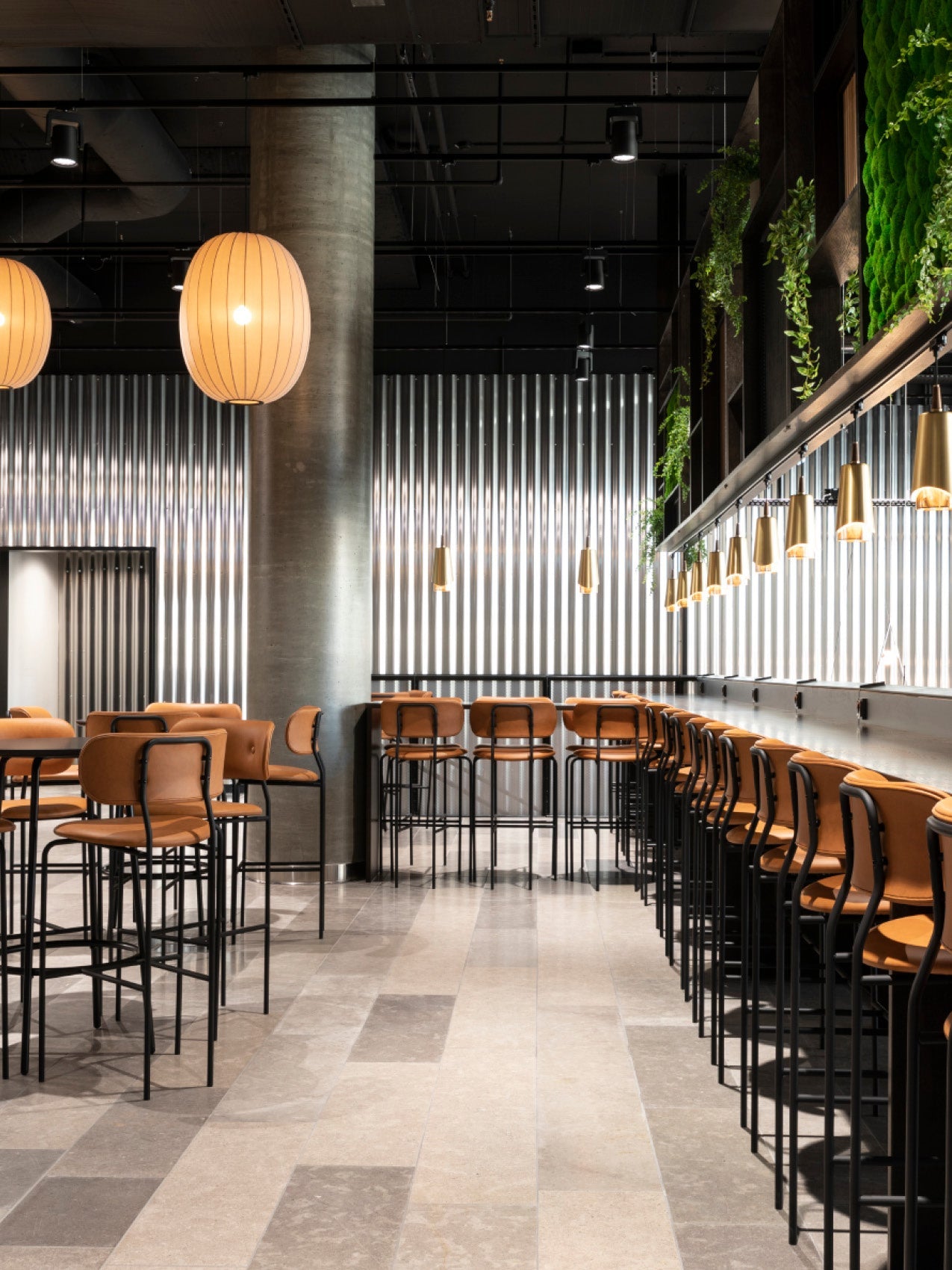 Modern cafe interior with tan leather high stools and black metal frames, large round paper pendant lights, corrugated metal