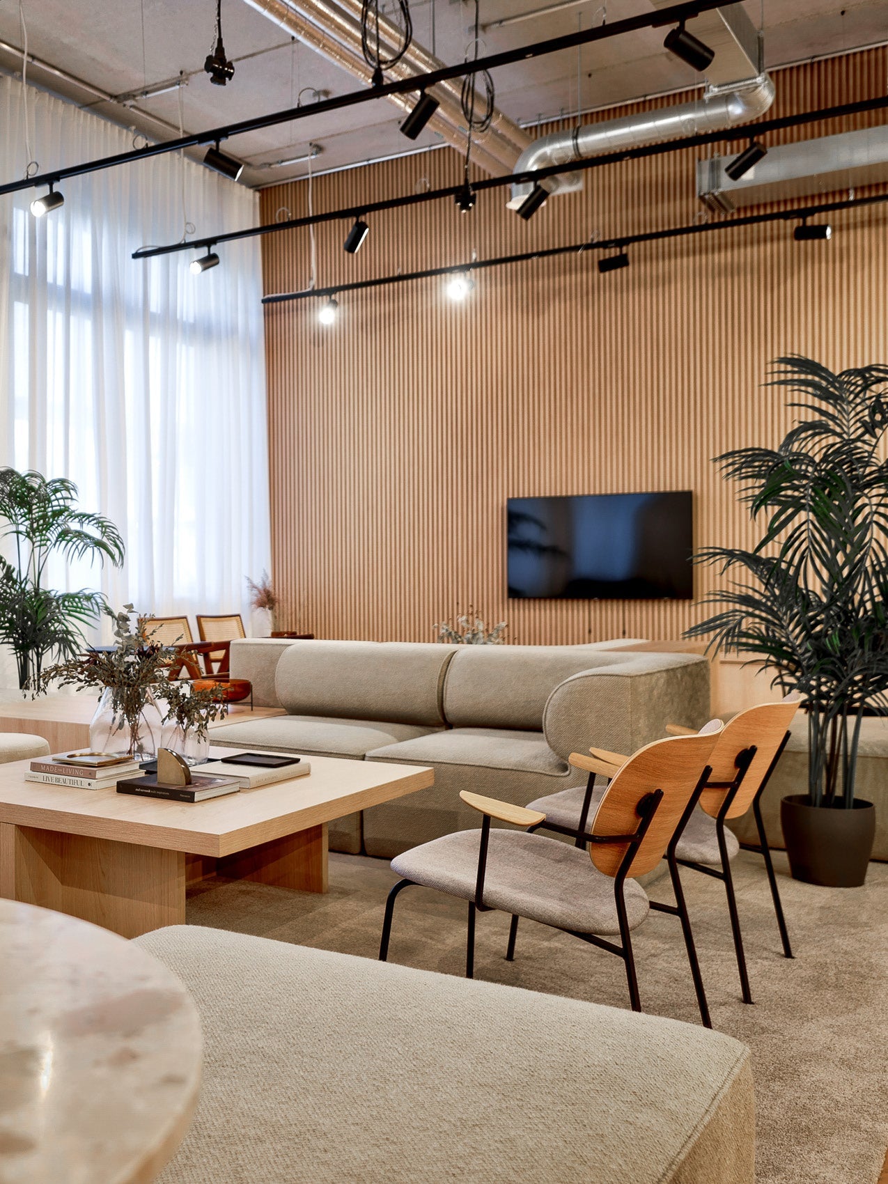 Scandinavian lounge with beige curved sofa, light wood coffee table, two wooden-back chairs, vertical wood slat wall and