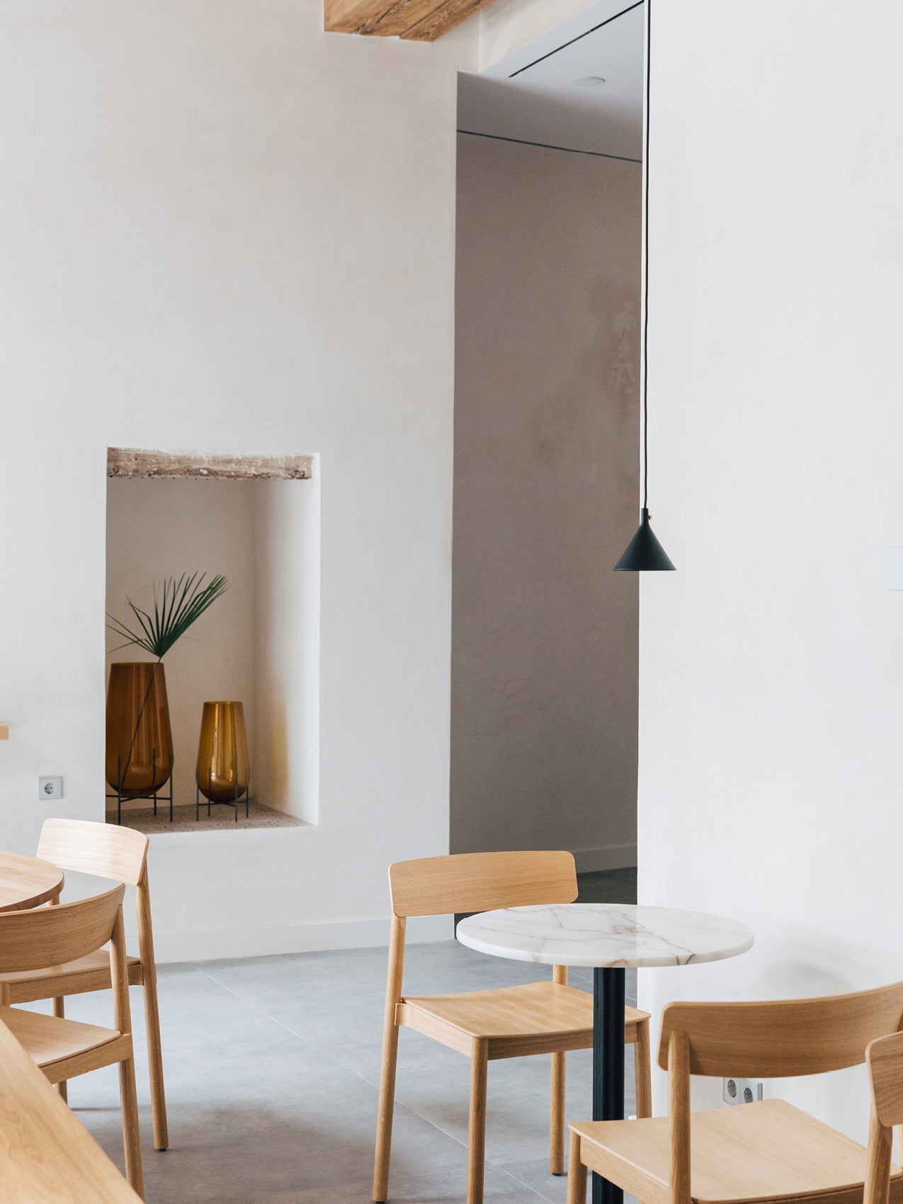 Minimal dining area with light oak chairs, round white marble table and black cone pendant; recessed niche with amber glass