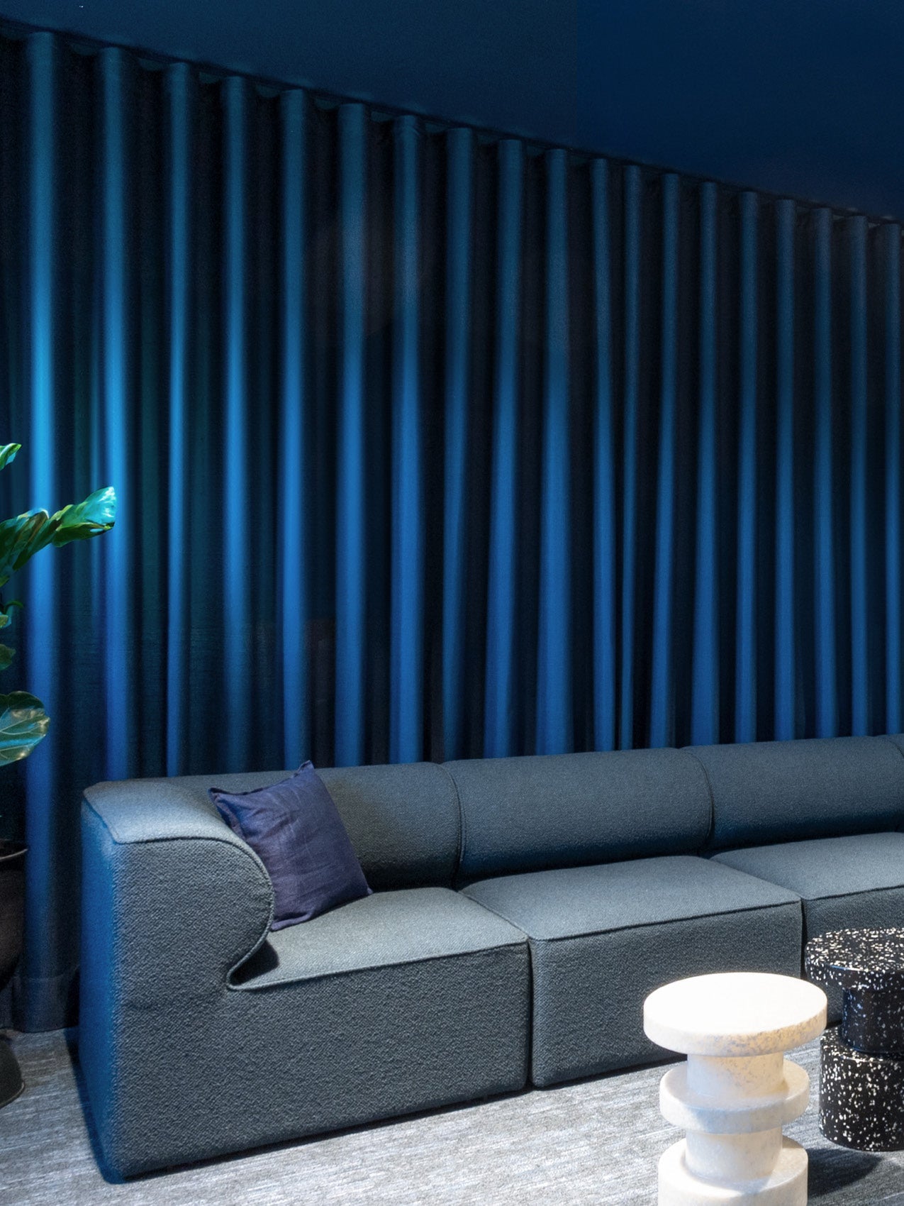 Dark blue modular fabric sofa with matching cushion, textured navy curtains and round white marble and black terrazzo side