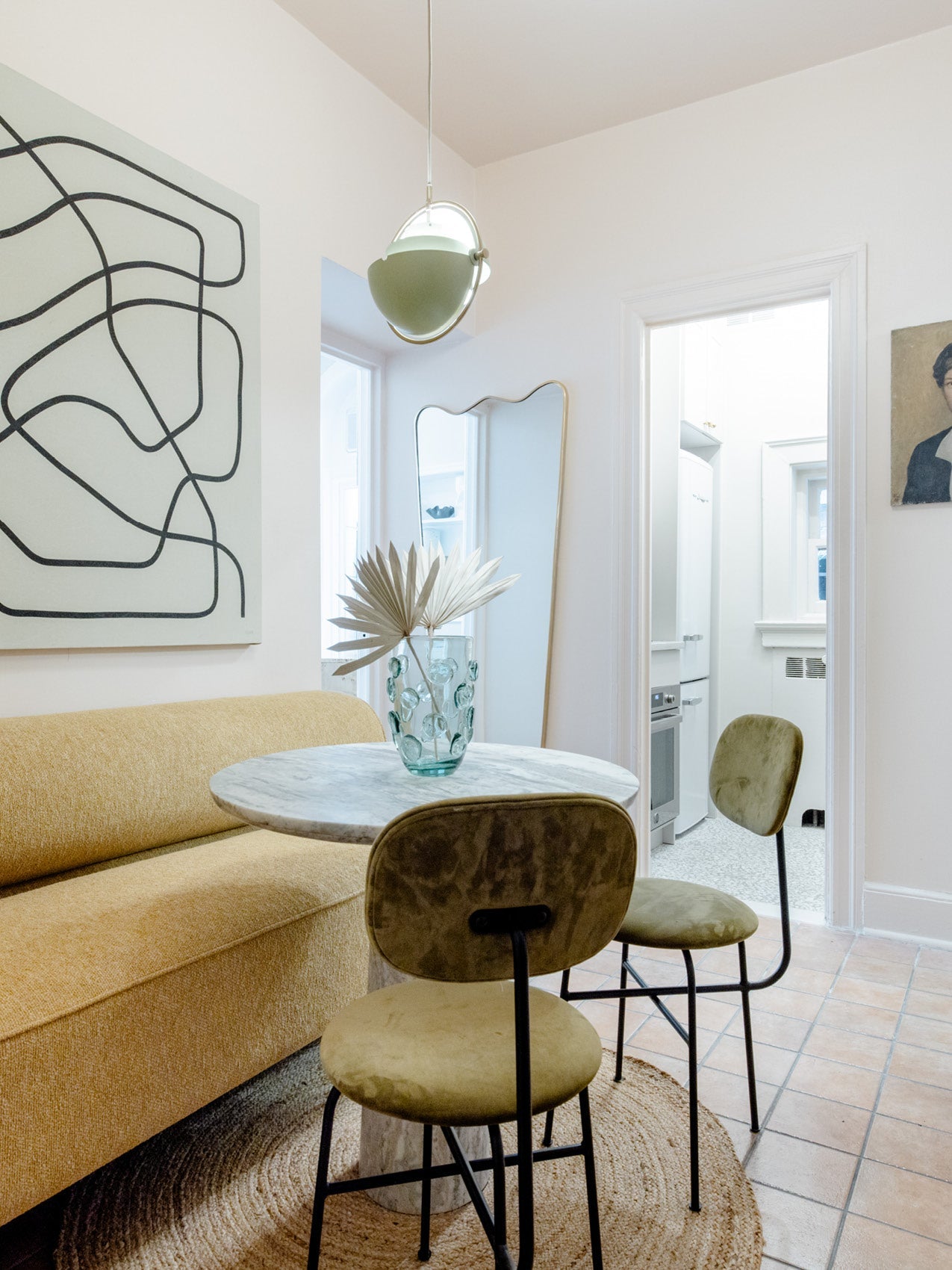 Cozy dining nook with mustard upholstered bench, round marble table, green velvet chairs and glass vase centerpiece