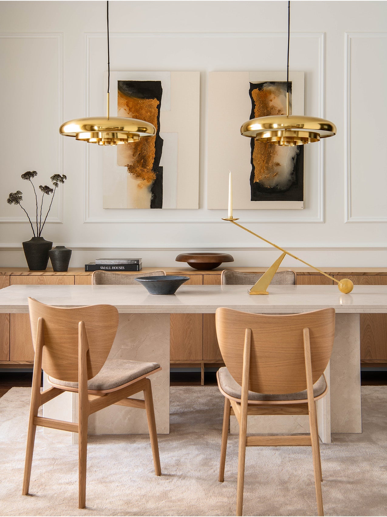 Dining room with marble-top table, oak chairs, twin polished brass pendant lights and abstract wall art