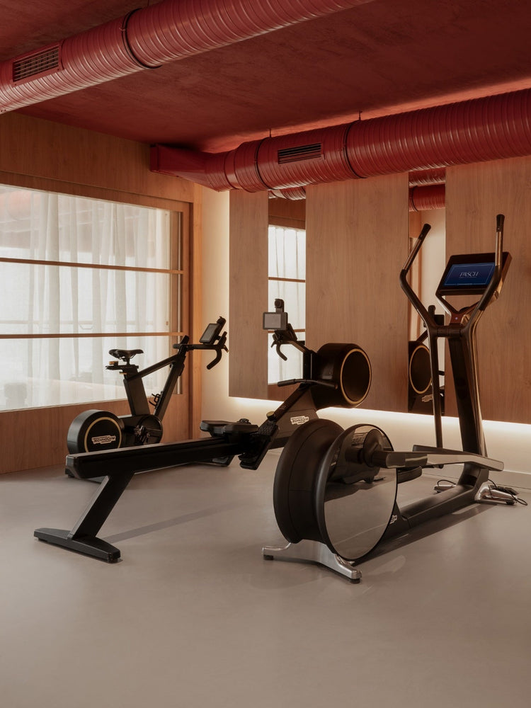 Minimal gym interior with black rowing machine, exercise bike and elliptical against wood panels, red exposed ductwork above
