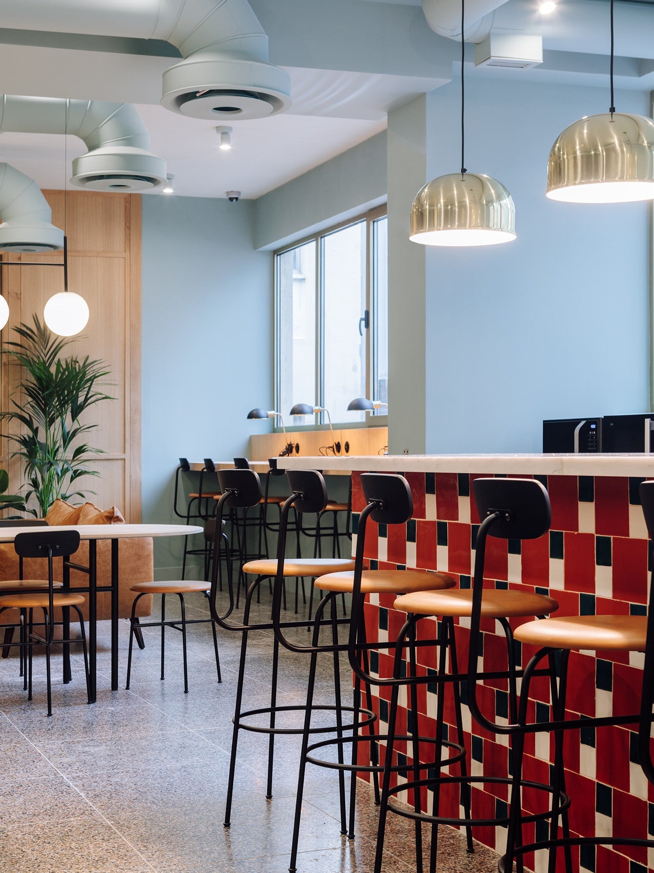 Modern café interior with black metal bar stools with tan leather seats at a red-and-white tiled counter and brass dome