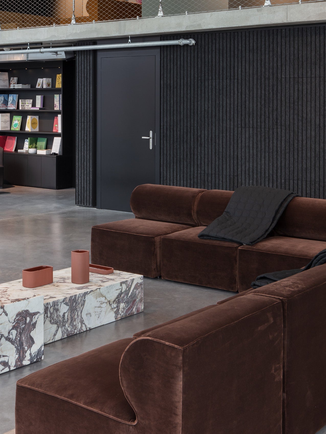 Brown velvet modular sofa with rounded armrests, marble low coffee table and terracotta accessories in modern showroom.