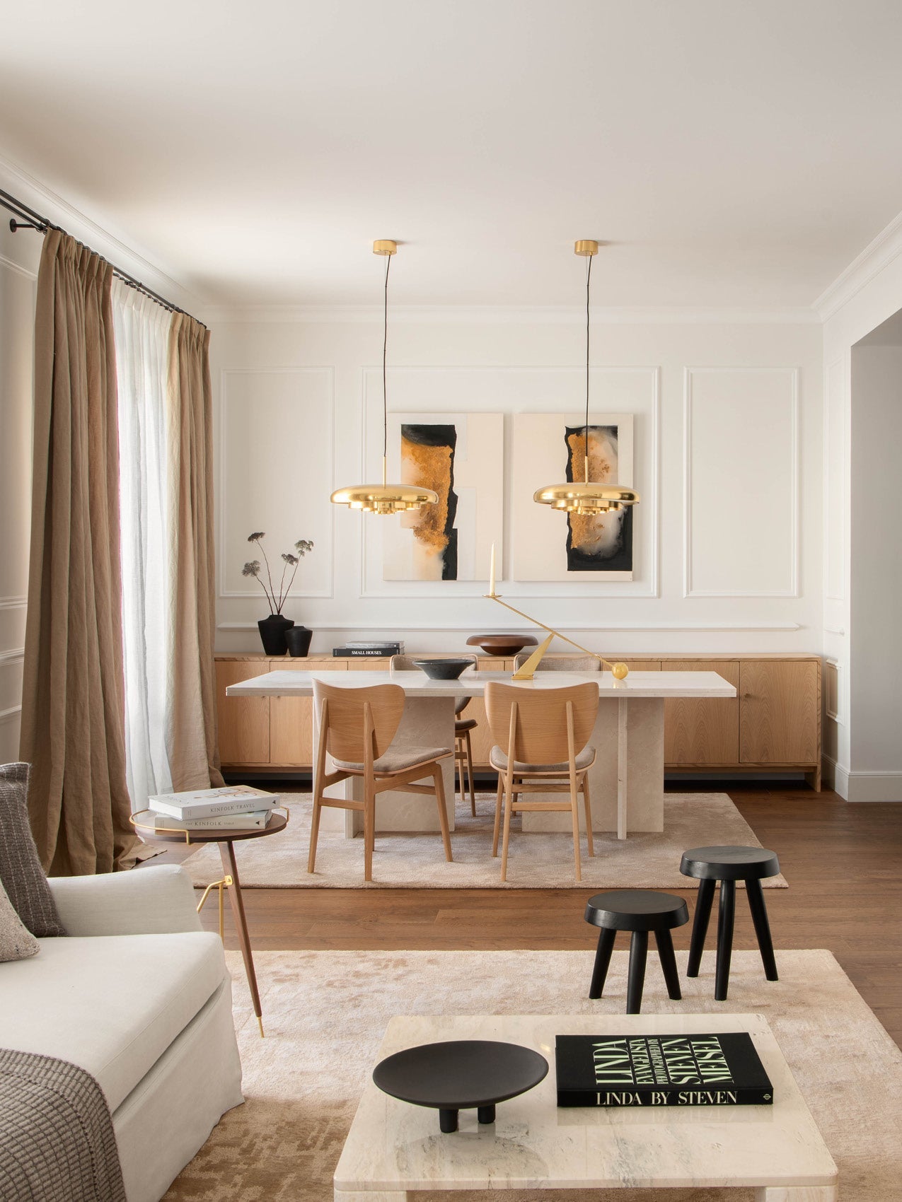 Minimal dining room with beige tones, marble table, light wood chairs, brass pendant lamps and abstract wall art