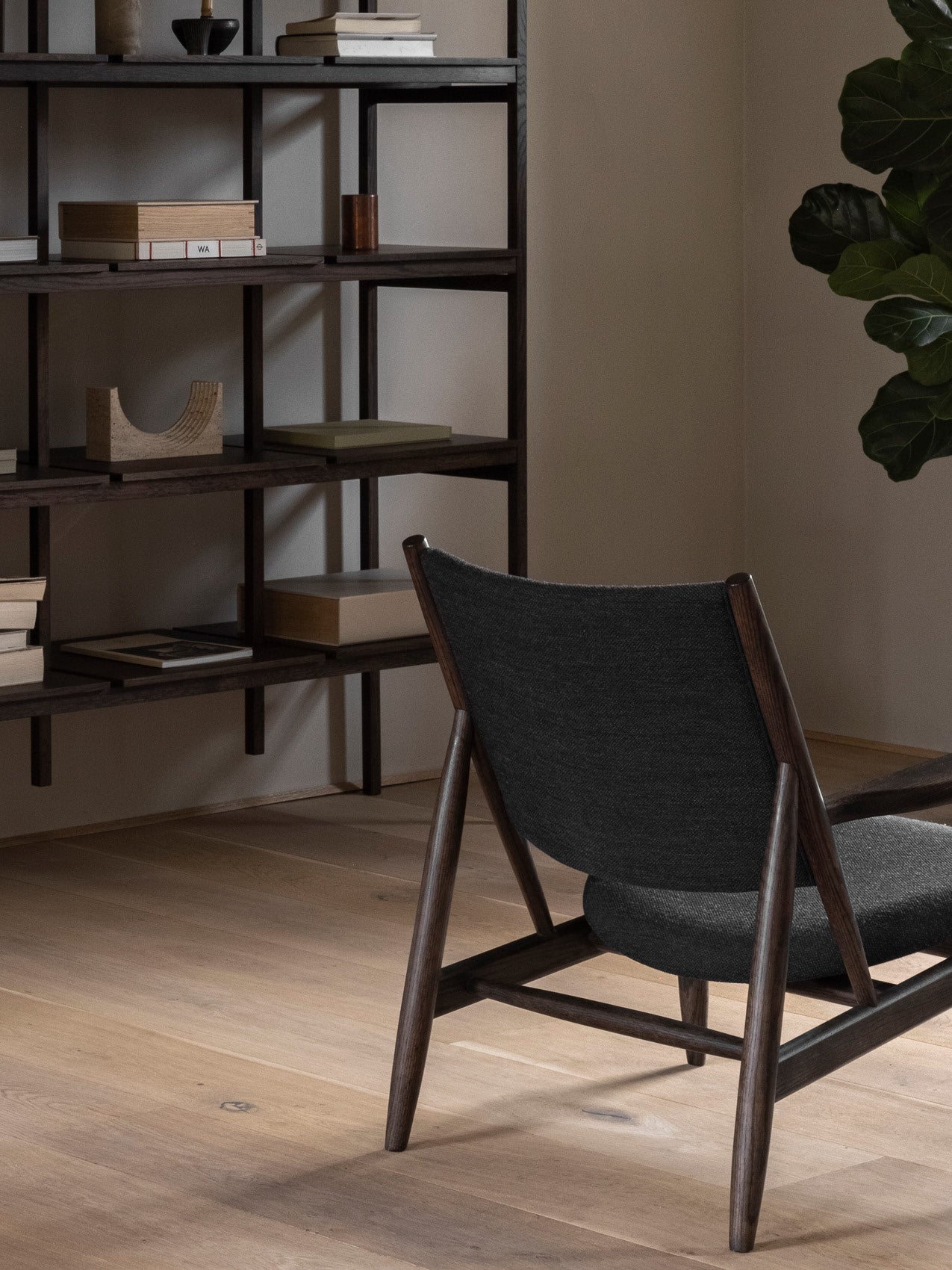 Dark wood lounge chair with charcoal upholstered seat and back in front of a matching open shelving unit and wooden floor