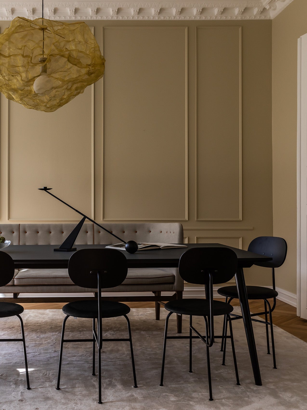Dining room with black minimalist table and chairs, beige tufted bench, sculptural gold fabric pendant and angled black lamp